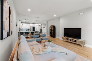 A modern living room with a sofa, chairs, a TV, and a kitchen in the background. - Cozy 2-bedroom townhome in peaceful Austin with AC (Austin)