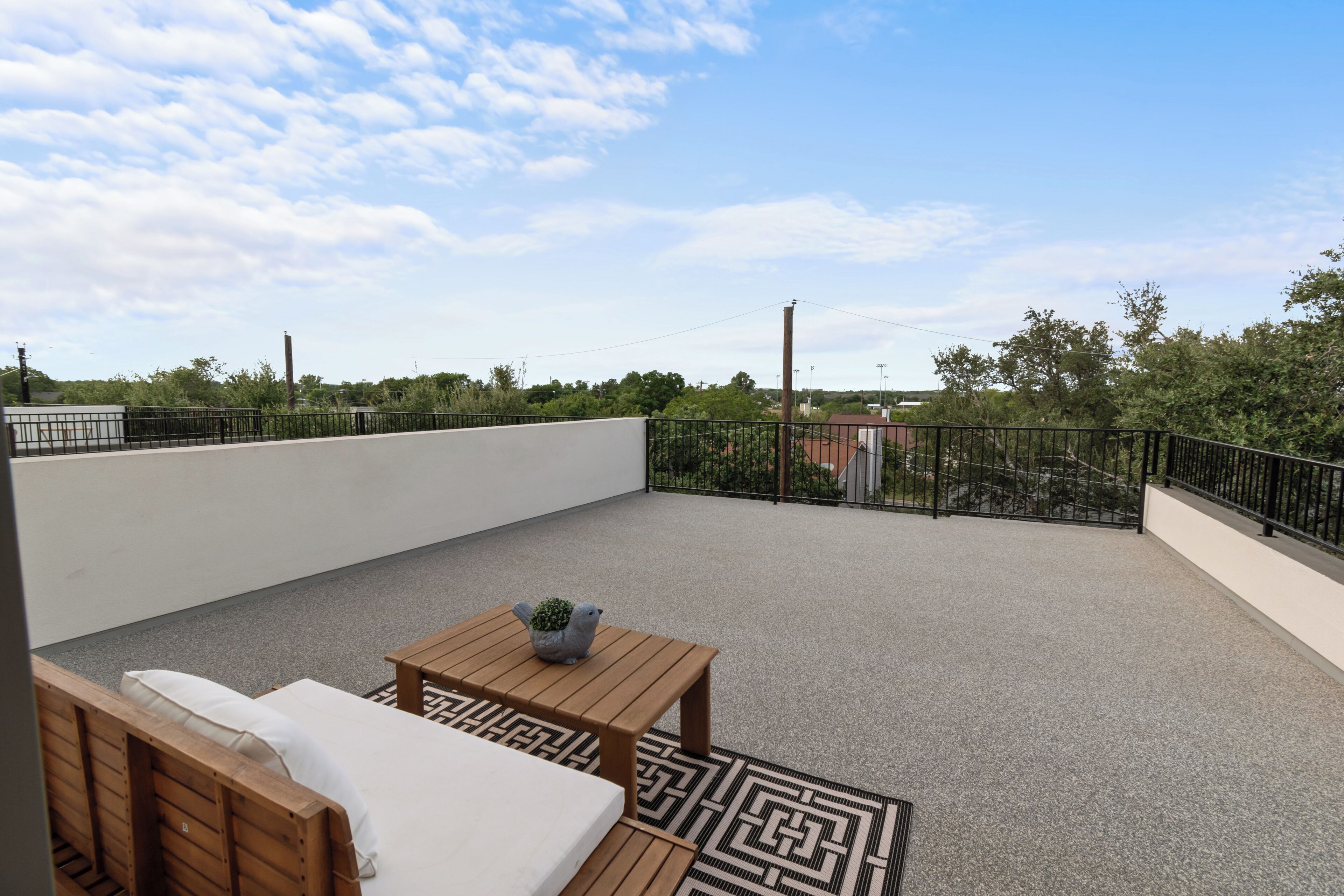 A rooftop terrace with a wooden bench, a small table with a potted plant, and a patterned rug.