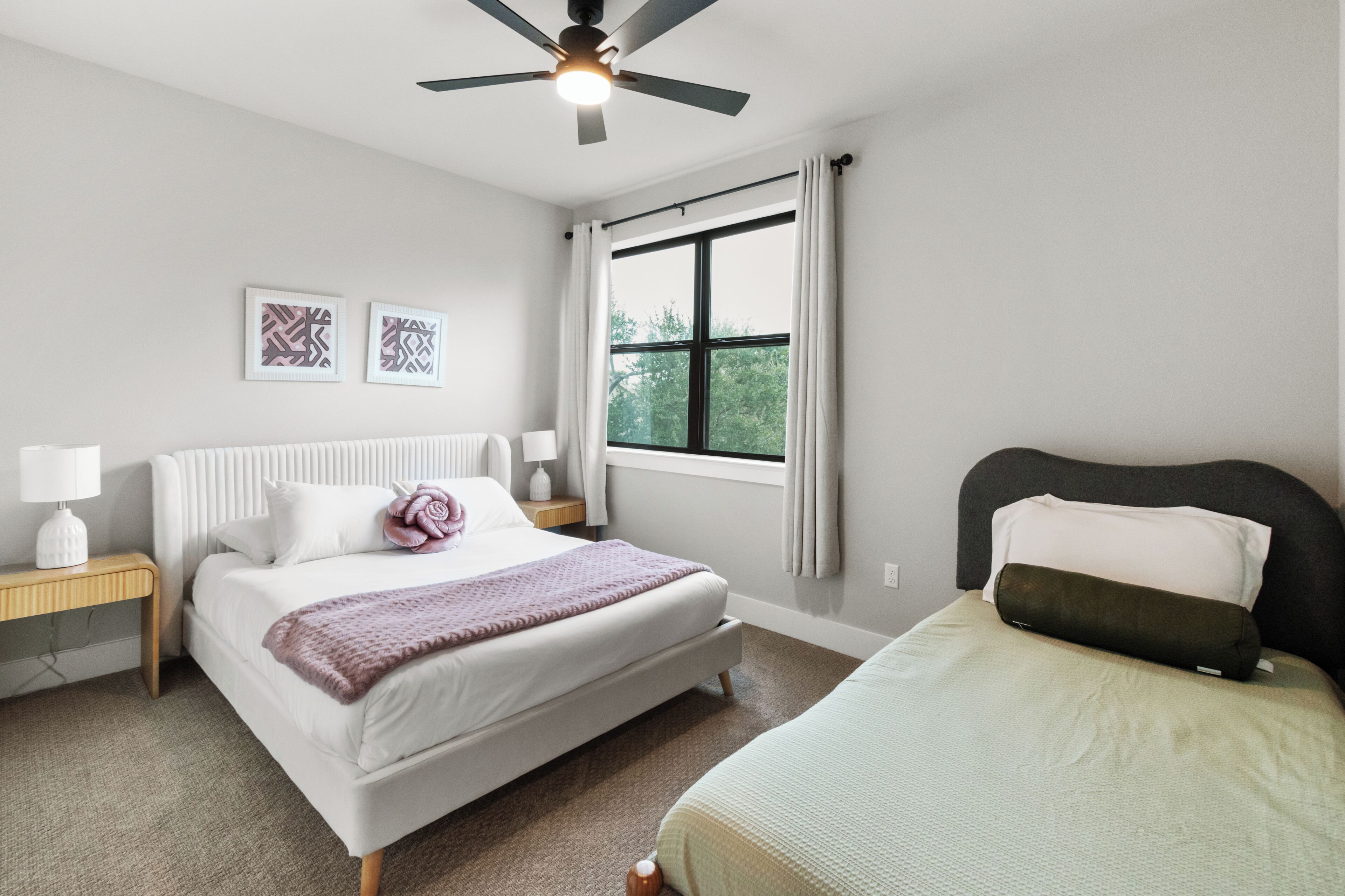 Ein Schlafzimmer mit einem Bett, einem Nachttisch, einer Lampe, einem Deckenventilator und einem Fenster mit Vorhängen.
