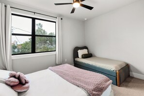 Ein Schlafzimmer mit Bett, Fenster, Deckenventilator und Blick ins Freie.