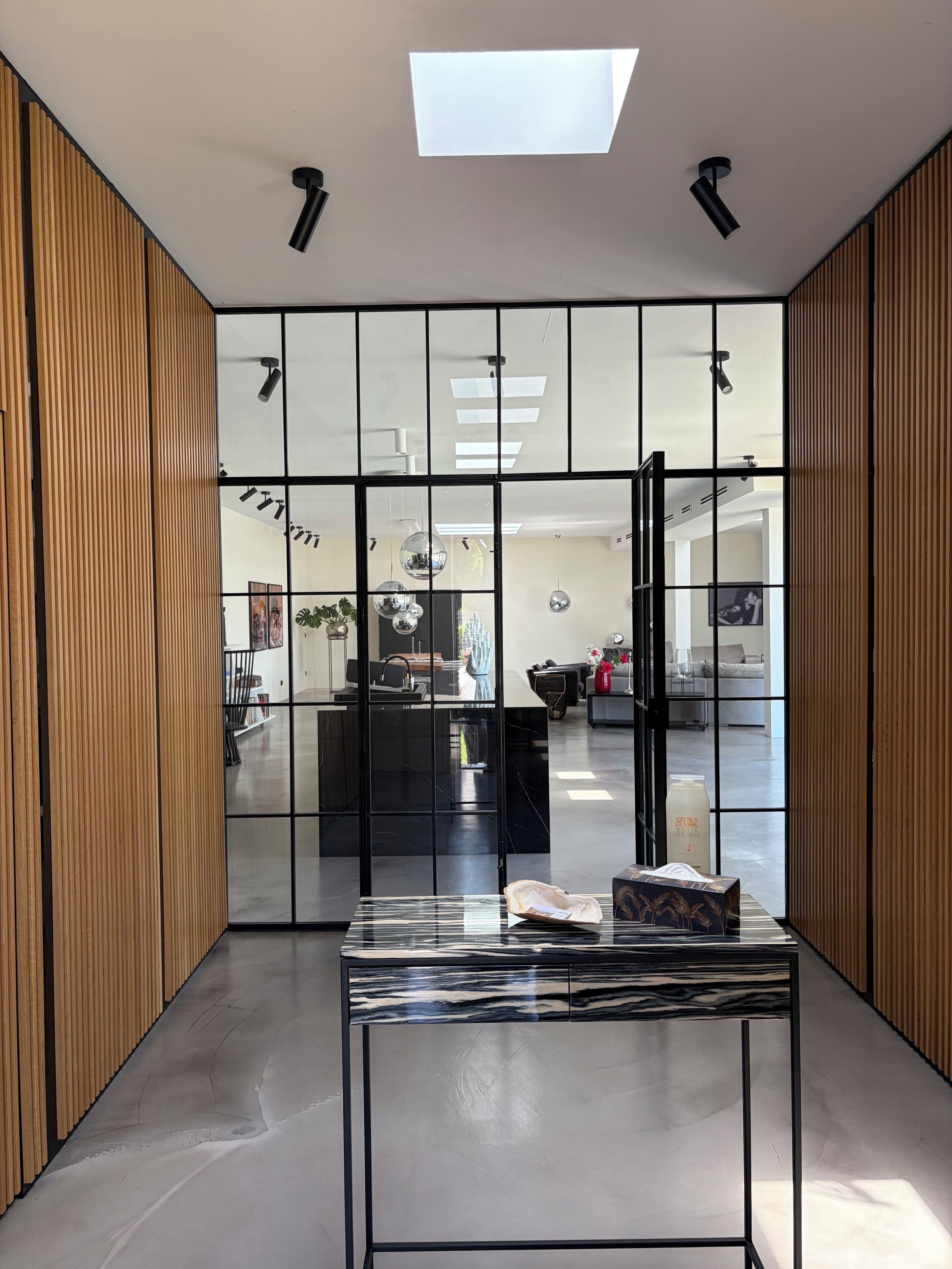 A modern interior with a glass partition, a marble-top table, and a skylight.