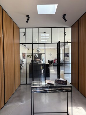 A modern interior with a glass partition, a marble-top table, and a skylight.