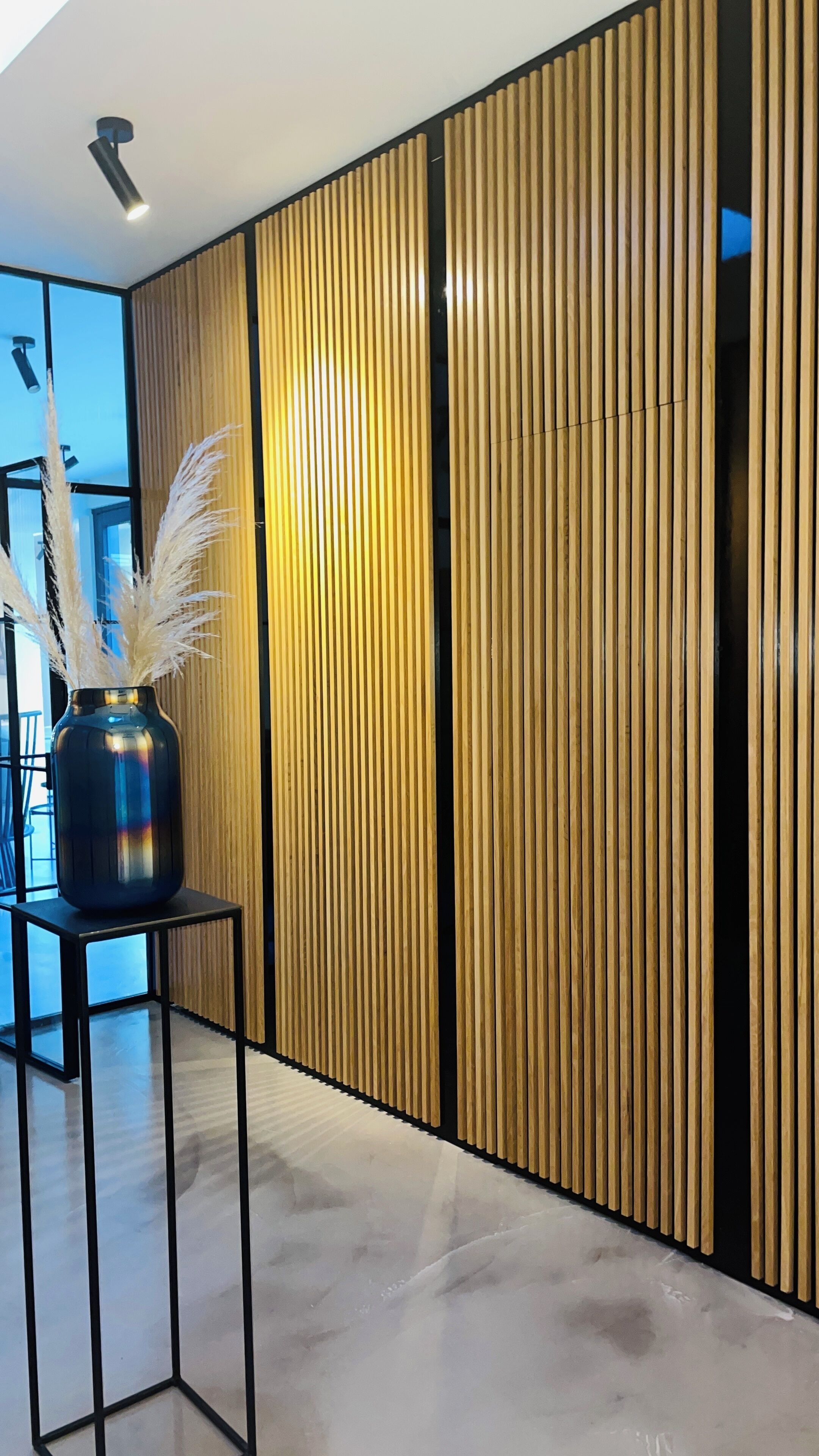 A modern interior with a wooden panel wall, a black metal table with a vase, and a polished floor.