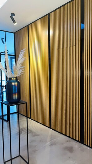 A modern interior with a wooden panel wall, a black metal table with a vase, and a polished floor.