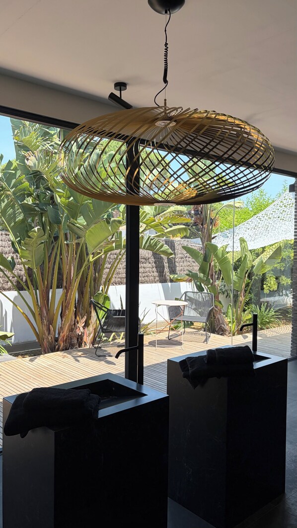 A modern interior with a ceiling fan, a large window with a view of tropical plants, and a black sink.
