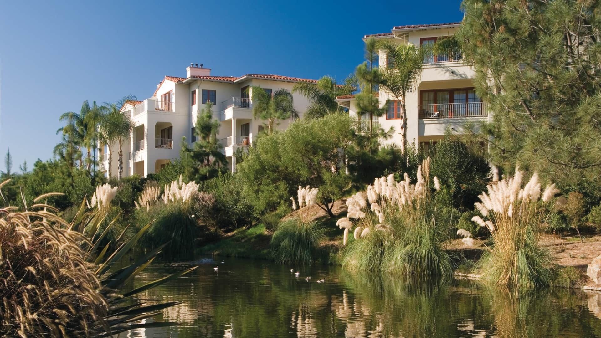 Ein Hotel mit mehrstöckigen Gebäuden, einem Gewässer im Vordergrund und umgebender Bepflanzung.
