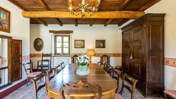 A dining room with a wooden table, chairs, and a chandelier. There are framed pictures on the walls and a large wooden cabinet.