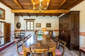 A dining room with a wooden table, chairs, and a chandelier. There are framed pictures on the walls and a large wooden cabinet.
