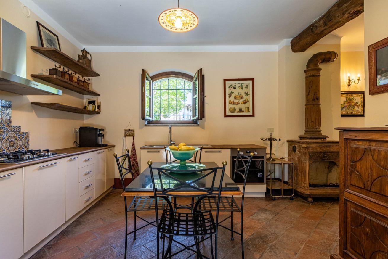 Een keuken met een eettafel, stoelen, een fornuis en een raam met openslaande luiken.