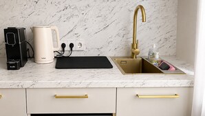 A kitchen with a marble countertop, a gold faucet, a coffee maker, a kettle, and a drawer with dishes. - Sunlay City (Rīga)