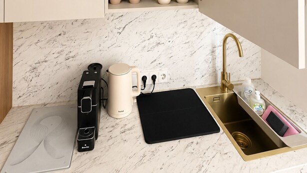 A kitchen with a marble countertop, a black induction cooktop, a beige coffee maker, and a gold faucet. - Sunlay City (Rīga)