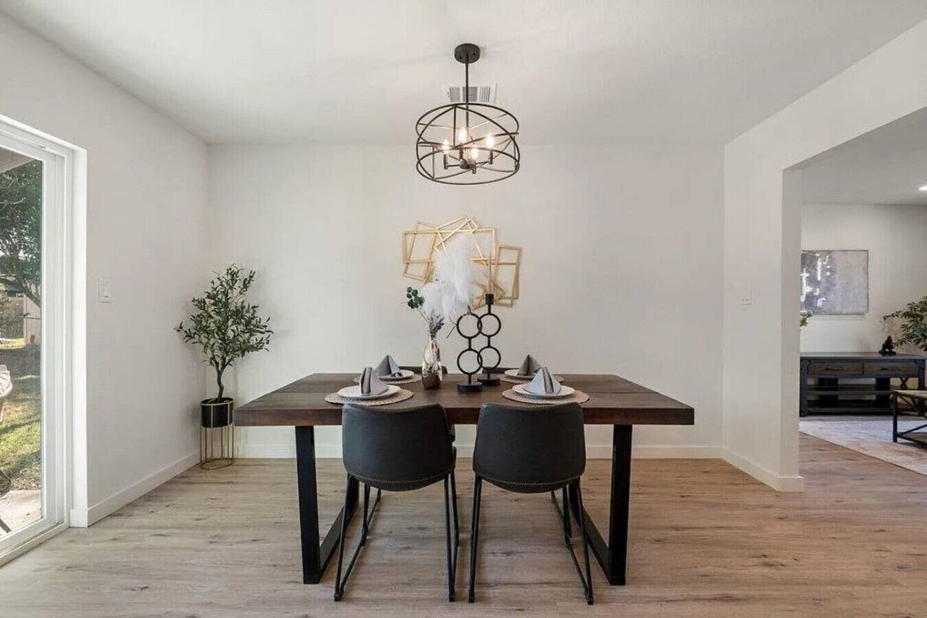 A dining area with a wooden table, two black chairs, a modern pendant light, and a potted plant.