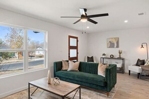 Een moderne woonkamer met een groene bank, een bijzettafeltje, een plafondventilator en uitzicht op het omliggende landschap.