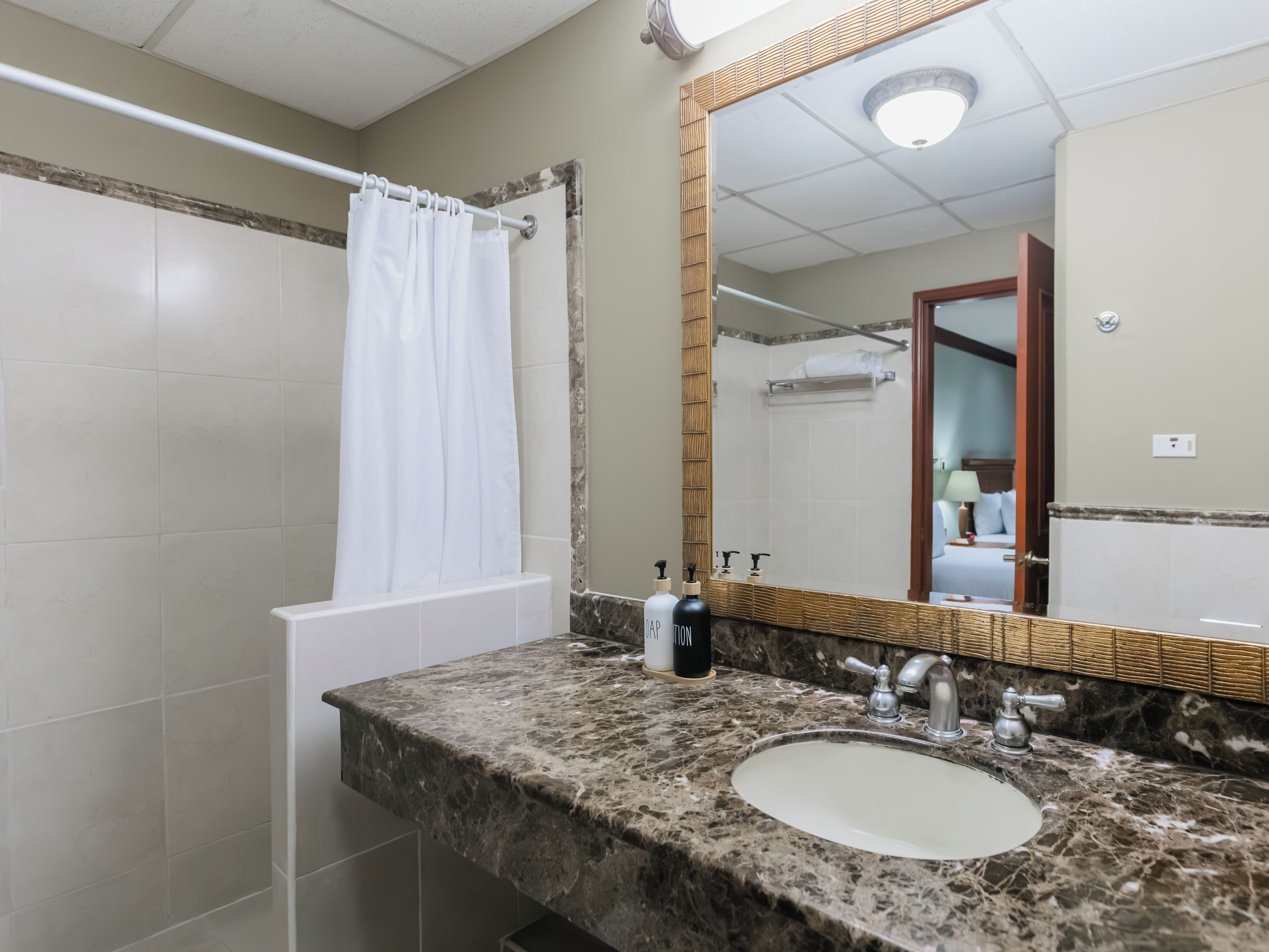 A bathroom with a marble sink, a mirror with a wooden frame, and a shower curtain.