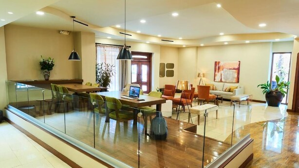 A modern kitchen with a glass partition, a dining area with chairs, and a living space with a sofa and a lamp. - Suites Las Palmas Hotel & Apartments (San Salvador)