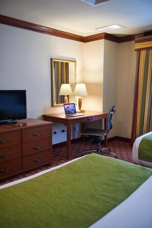 Ein Hotelzimmer mit einem Bett, einem Schreibtisch mit Computer, einem Fernseher und einem Sessel.