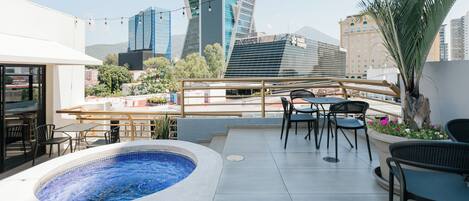Una terraza en la azotea con hidromasaje, mobiliario exterior y vistas a un horizonte urbano.