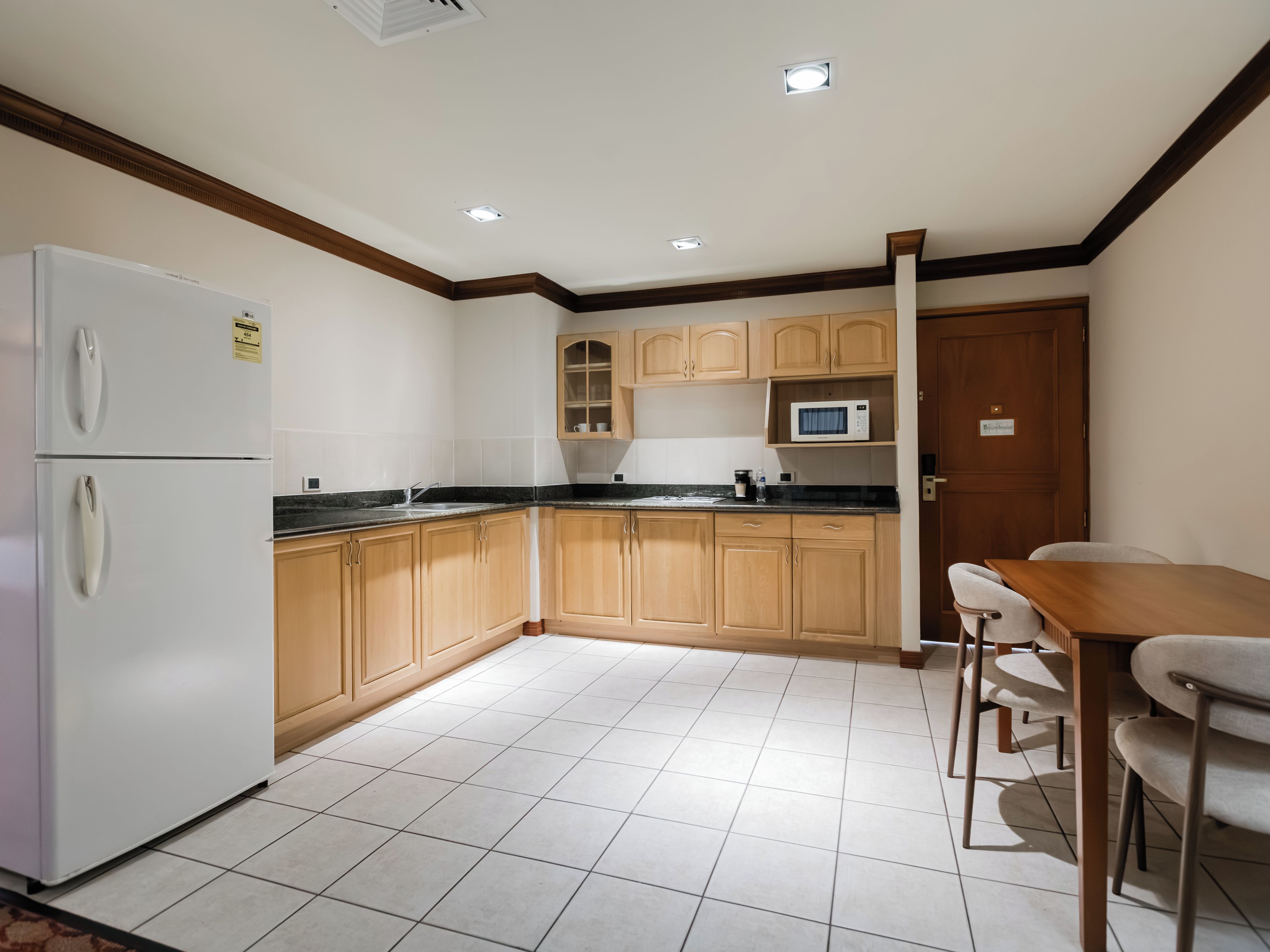 Una cocina con armarios de madera, un refrigerador blanco, un microondas y un comedor con mesa y sillas.
