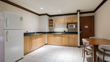 Una cocina con armarios de madera, un refrigerador blanco, un microondas y un comedor con mesa y sillas.