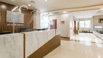 A hotel reception area with a marble counter, wooden paneling, and a view of the adjacent room.