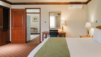 Quarto de hotel com cama, mesas de cabeceira, espelho, porta e vista para o quarto vizinho.