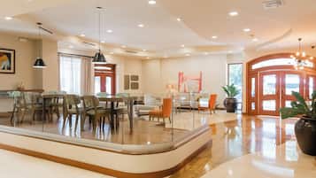 A hotel lobby with a dining area, seating, a reception desk, and a large potted plant.