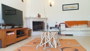 Una sala de estar con televisor, chimenea, mesa de centro de vidrio y sofá.