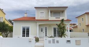 A two-story building with a red-tiled roof, white exterior walls, and a central entrance with a door and windows. - Villa Amoreira: The Perfect Retreat (Óbidos)