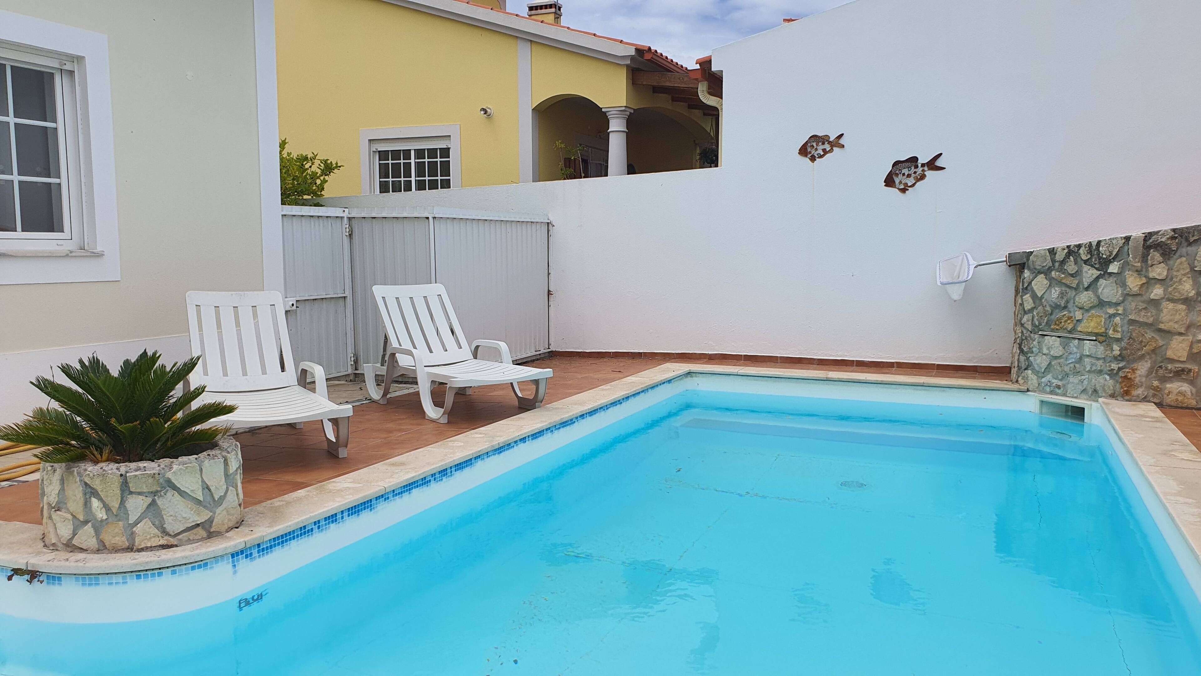 Une piscine entourée de chaises longues blanches et agrémentée d’une plante en pot.