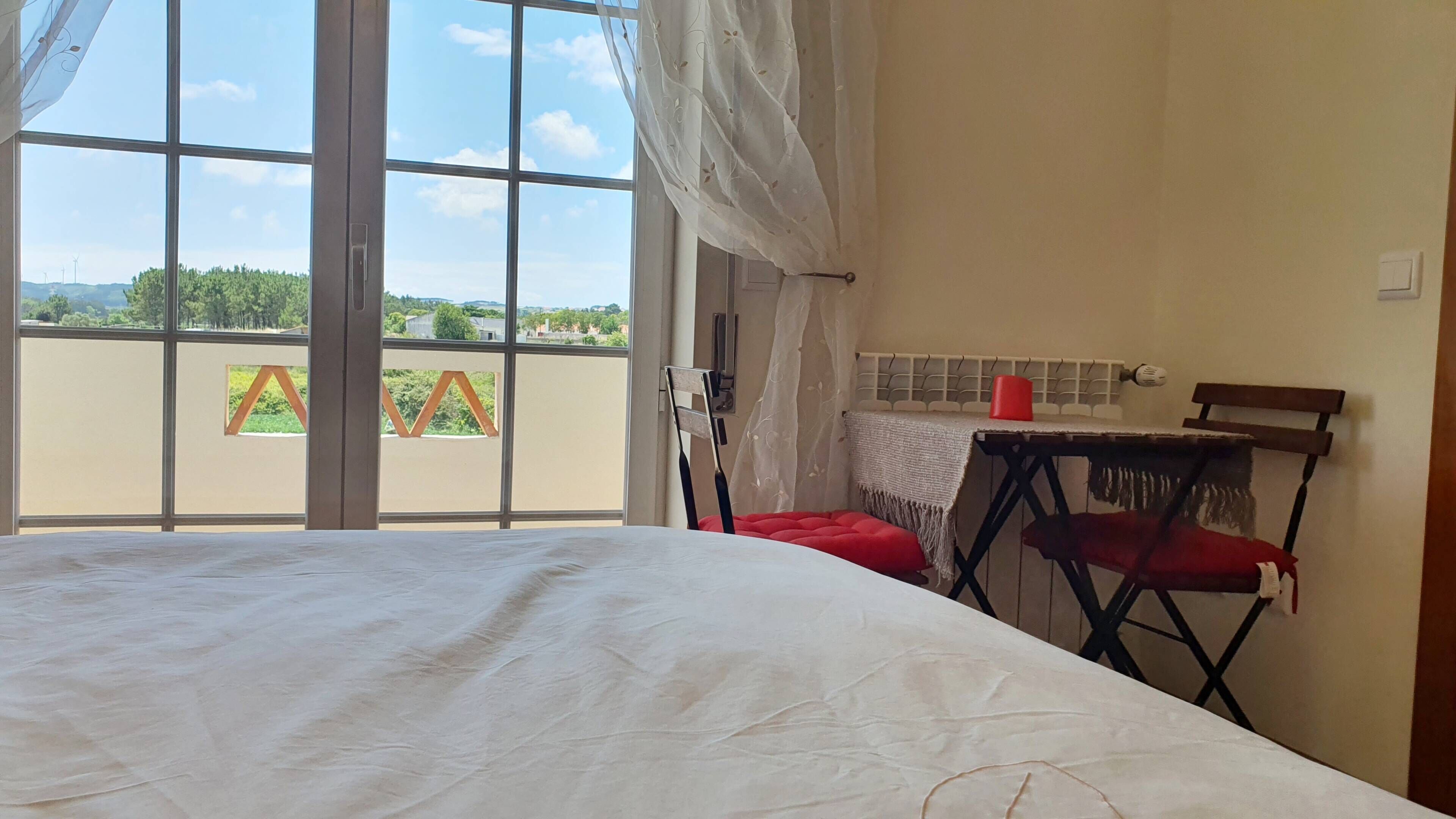 A room with a bed, a chair, a table, and a view through a window.
