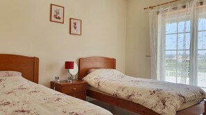 A bedroom with two beds, a bedside table with a lamp, and a window with a view. - Villa Amoreira: The Perfect Retreat (Óbidos)