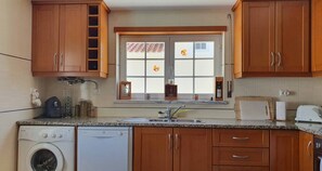 A kitchen with wooden cabinets, a window with a view, a washing machine, and a toaster. - Villa Amoreira: The Perfect Retreat (Óbidos)