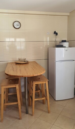 Eine Küche mit einem Holztisch, zwei Hocker, einem Kühlschrank und einer Wanduhr.