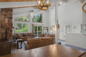 A spacious living room with a large wooden table, a stone wall, and a ceiling chandelier. - Steps to Heavenly | Mountain Chalet w/ Hot Tub (South Lake Tahoe)