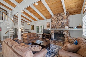 A spacious living room with a fireplace, a television, and a stone accent wall. - Steps to Heavenly | Mountain Chalet w/ Hot Tub (South Lake Tahoe)