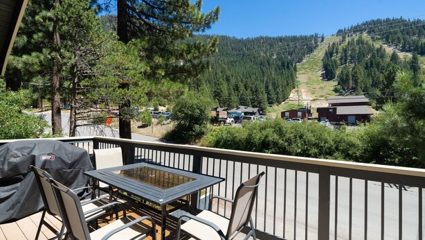 Ein Balkon mit Tisch und Stühlen, der auf eine Berglandschaft mit Häusern und klarem Himmel blickt.