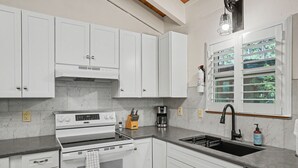 Eine moderne Küche mit weißen Schränken, einem eingebauten Backofen, einer Kaffeemaschine und einem Fenster mit Jalousien.