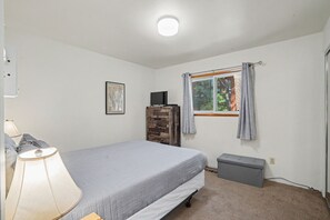 A bedroom with a bed, a nightstand, a lamp, a dresser, a window with curtains, and a small bedside table. - Steps to Heavenly | Mountain Chalet w/ Hot Tub (South Lake Tahoe)