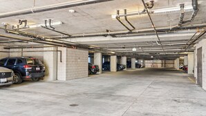 Eine mehrgeschossige Parkgarage mit Betonpfeilern, Leitungen an der Decke und einigen abgestellten Fahrzeugen.