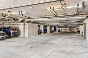 A multi-level parking garage with concrete pillars, overhead pipes, and a few parked vehicles. - Luxury Midtown Stay • Pool • Hot Tub • Near Downtown • King Bed (Phoenix)