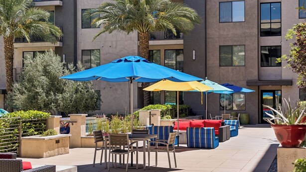 Eine moderne Außenpatio-Terrasse mit Sitzgelegenheiten und Sonnenschirmen, umgeben von einem Gebäude mit mehreren Balkonen und Fenstern.