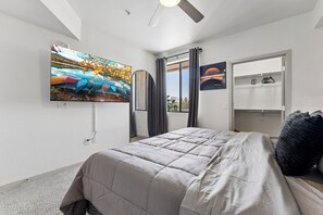 A bedroom with a bed, a television mounted on the wall, a window with curtains, and a door with a coat rack. - Luxury Midtown Stay • Pool • Hot Tub • Near Downtown • King Bed (Phoenix)