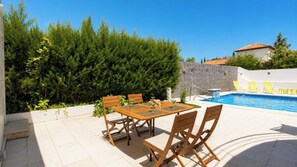 A poolside area with a table and chairs, a swimming pool, and a stone wall.