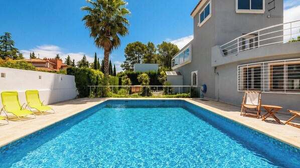 A rectangular swimming pool with clear blue water, surrounded by a white wall and a balcony with a railing.