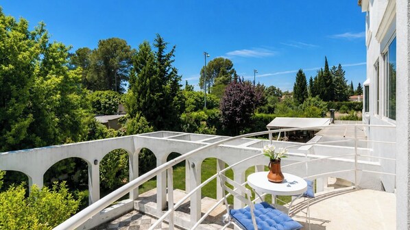 A balcony with a white railing, a round table with a vase, and a blue cushion.
