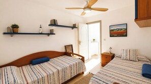 A bedroom with two beds, a ceiling fan, a door leading outside, and a small bedside table with a lamp.