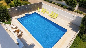 A rectangular swimming pool with a tiled deck, surrounded by a low stone wall, and equipped with several lounge chairs. - La Luna Albolote by Ruralidays (Granada)