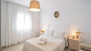 Ein Hotelzimmer mit einem Bett, zwei Nachttischen, einer Lampe, einer Wanduhr und einem Fenster mit Vorhängen.