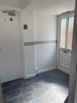 A hallway with a white door marked '1' and a fire door sign, a window with a notice sign, and a tiled floor.