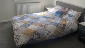 Et soveværelse med en seng, et vindue med persienner, en radiator, et natbord og billedkunst på væggen.